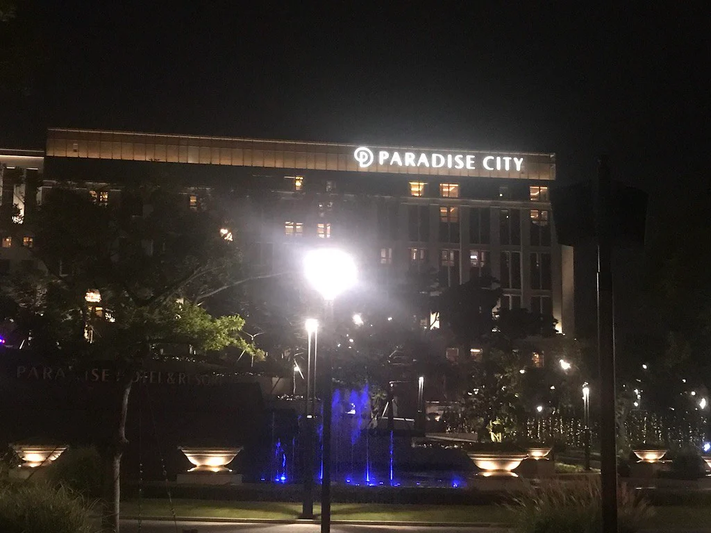 PARADISE CITY 간판이 켜진 호텔 건물의 야간 외관과 앞쪽 조경